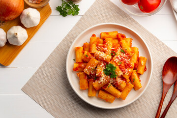 Rigatoni macaroni with fresh tomatoes sauce in white plate.topped with parmesan cheese and parsley.Top view.