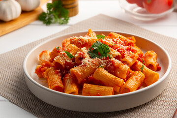 Rigatoni macaroni with fresh tomatoes sauce in white plate.topped with parmesan cheese and parsley.