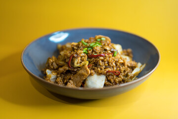 Spicy fried rice with pork and vegetables in blue bowl on yellow background