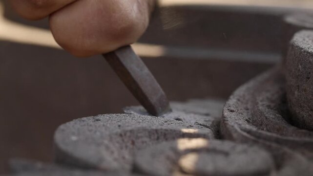 Close up of artisan hands carving stone with chisel and hammer. Skilled sculptor creating detailed architectural ornament. Traditional manual craftsmanship process in a workshop setting.

