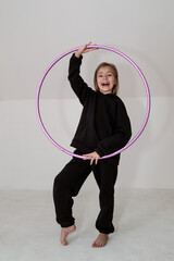A young rhythmic gymnast in a black tracksuit performs elements with a hoop