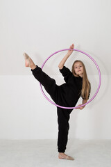 A young rhythmic gymnast in a black tracksuit performs elements with a hoop