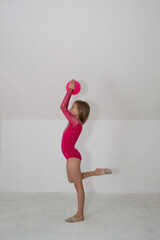 A young rhythmic gymnast in a bright pink leotard is training with a ball