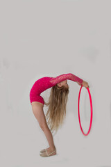 A young rhythmic gymnast in a bright pink leotard is training with a hoop