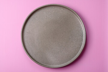 An empty round ceramic plate on a pink background as a kitchen utensil. An empty plate