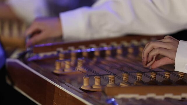 Close-up of musician's hands playing the Qanun. The artist plucks strings and adjusts tuning levers on this traditional Middle Eastern string instrument during a live musical concert performance.

