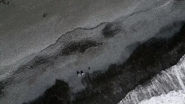 Cinematic aerial drone view of Reynisfjara Black Sand Beach, Reynisdrangar basalt sea stacks and green coastal cliffs in Iceland 4K.