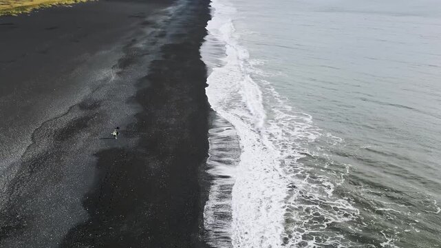 Cinematic aerial drone view of Reynisfjara Black Sand Beach, Reynisdrangar basalt sea stacks and green coastal cliffs in Iceland 4K.