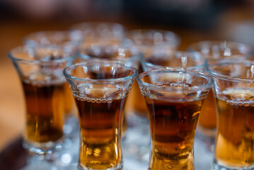 A cluster of small flared shot glasses holds amber liqueur in Funchal, rims beaded with bubbles, sharp front focus and creamy bokeh suggest a festive tasting mood.