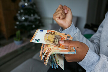 A wad of euro banknotes held by the hands of a light-skinned African American woman celebrating that she has that money