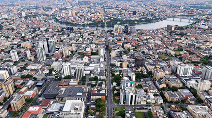 Fototapeta premium Cityscape Aerial View: An expansive aerial perspective captures a bustling city, showcasing a grid of buildings stretching towards the horizon, interspersed with roads, bridges, and a serene lake.