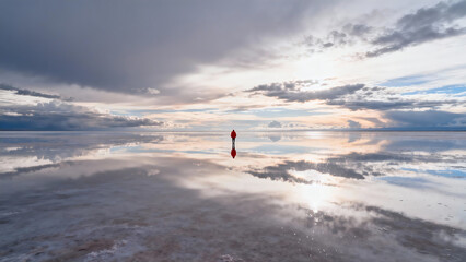 Red-clad figure stands in salt flat��s sky reflection