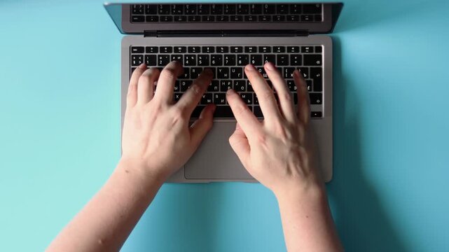 Hands typing on a laptop keyboard against a blue background. Flatlay concept, advertising remote work