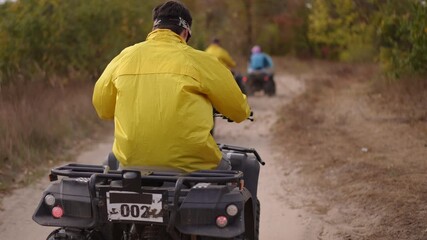 rear view rider yellow jacket atv trail kicking up dust along rural dirt path through autumn forest, helmeted adult navigating winding track with friends ahead,
