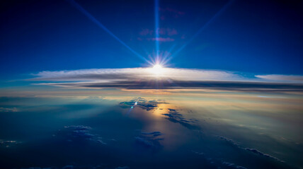 Sunlight bursting through clouds over the ocean, aerial view. 60 chars.