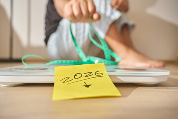 Person sitting on floor with a scale displaying 2026 target for weight loss