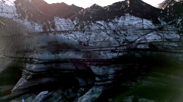 Cinematic aerial drone flight through Katla ice cave tunnel showing blue ice with black volcanic ash veins and green mossy mountains in Iceland 4K.