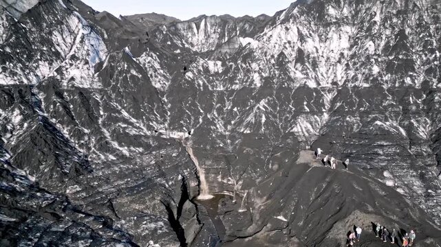 Cinematic aerial drone flight through Katla ice cave tunnel showing blue ice with black volcanic ash veins and green mossy mountains in Iceland 4K.