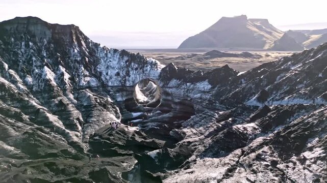 Cinematic aerial drone flight through Katla ice cave tunnel showing blue ice with black volcanic ash veins and green mossy mountains in Iceland 4K.