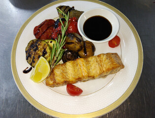 Baked sturgeon steaks with fresh salad greens, basil leaves and cherry tomatoes on a large white plate. delicious and healthy food for kids and adults. diet food. grilled vegetables next to the fish