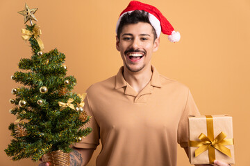 cheerful brazilian man with gift box present in beige studio background. christmas, gift box concept.