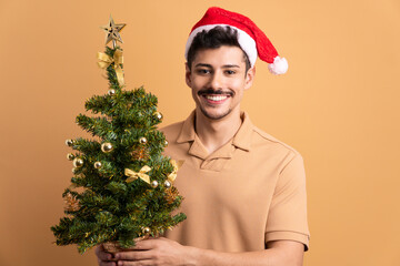 joyful brazilian man with christmas tree in beige background. christmas, holiday, celebration concept.