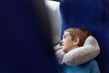Young passenger using neck pillow to rest peacefully while seated by window on high-speed express train. Travel comfort and quiet relaxation during journey. Copy space.