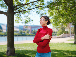 Woman in glasses and red turtleneck, dressed in business style, stands in center of Frankfurt, surrounded by modern buildings and urban life, embodying professionalism and confidence