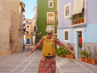 Woman in dress strolls through colorful streets of Spanish coastal town of La Vila Joiosa . sunny winter atmosphere highlights charm of Mediterranean architecture and quiet seaside life, back view