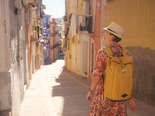 Woman in dress strolls through colorful streets of Spanish coastal town of La Vila Joiosa . sunny winter atmosphere highlights charm of Mediterranean architecture and quiet seaside life, back view
