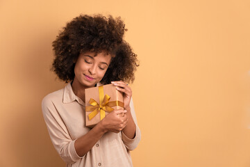 happy black woman with gift box present in all beige colors. christmas, holidays, festivity concept.