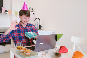 Young man video chatting with family on his birthday, smiling and joyful as he connects with loved ones from home, celebrating special day with warmth and connection