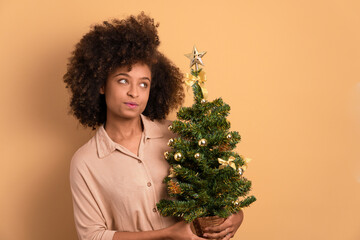 thoughtful afro brazilian woman with christmas tree in beige background. christmas, holiday, celebration concept.