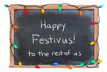 Happy Festivus handwritten in white chalk on a black chalkboard decorated with festive holiday...