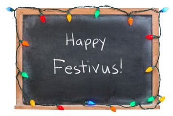 Happy Festivus handwritten in white chalk on a black chalkboard decorated with festive holiday...