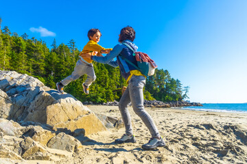 Mother catching son jumping from rock on beach in tofino