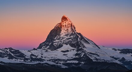 Majestic snow-covered alpine peak illuminated by soft sunrise or sunset glow against a colorful sky