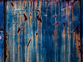 Full frame texture of old, peeling blue painted metal surface with prominent orange and brown rust streaks, abstract grunge background and industrial decay concept.