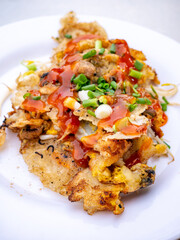 Crispy Thai Oyster Omelette (Hoi Tod) topped with sweet chili sauce and fresh spring onions on a white plate