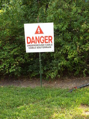 A close-up photograph of a "danger sign" posted outdoors against a backdrop of dense greenery.