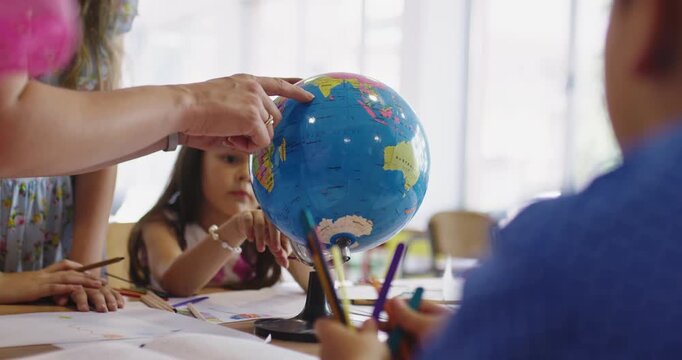 Teacher and elementary students learning geography with globe in classroom, curious children exploring world map together, social studies and global education for kids.