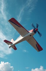 Red and white propeller plane flies against clear blue sky with thin clouds. Aircraft performs aerobatic stunt maneuver high above. Pilot enjoys hobby, recreational flight in small aircraft.