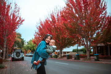 A joyful mother holds her child against a vibrant autumn backdrop, radiating love