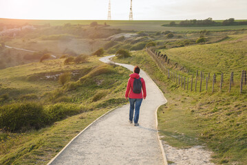 Woman walking alone on a winding clifftop path at sunset in spring
