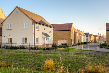 Newly built brick detached and semi-detached houses along a street in a housing development on the outskirts of city In England at sunset