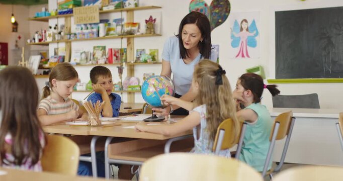 Teacher and elementary students learning geography with globe in classroom, curious children exploring world map together, social studies and global education for kids.