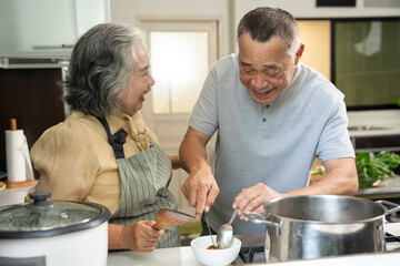Two senior adults enjoy cooking together in a cozy kitchen. One offers a spoonful of food while the other leans in to smell, capturing warmth, sensory joy, and togetherness in a home lifestyle setting