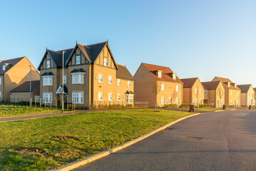 Newly built brick detached houses along a street in a new housing development at sunset
