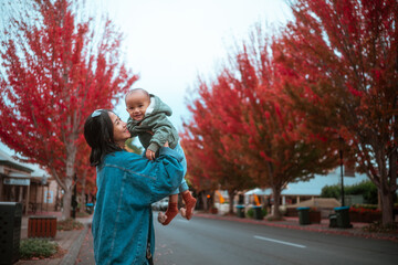Fototapeta premium A joyful mother lovingly holds her baby amid the stunning autumn foliage and colors