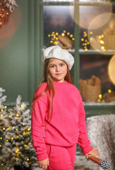 Cheerful little girl enjoying a festive winter scene outdoors. Child wearing a bright pink cozy outfit and a white beret. Close-up. Children's fashion and style concept.
